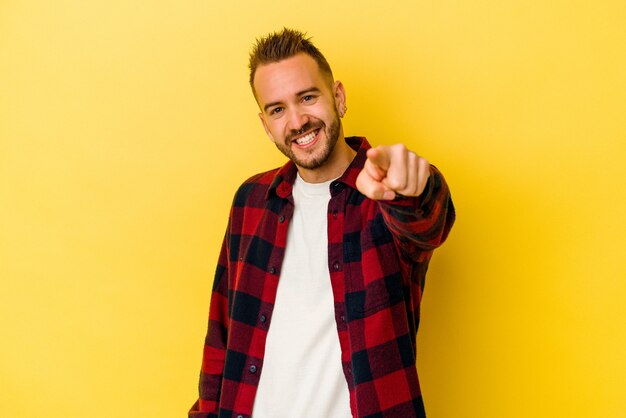 Jeune homme caucasien tatoué isolé sur fond jaune sourires joyeux pointant vers l'avant.