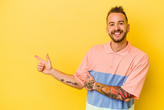 Jeune homme caucasien tatoué isolé sur mur jaune souriant joyeusement pointant avec l'index loin.