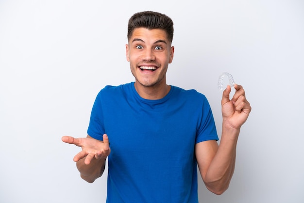 Jeune homme caucasien tenant des accolades invisibles isolé sur fond blanc avec une expression faciale choquée