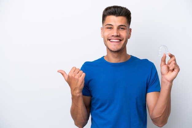 Jeune homme caucasien tenant des accolades invisibles isolé sur fond blanc pointant vers le côté pour présenter un produit