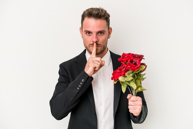Jeune homme caucasien tenant un bouquet de fleurs isolé sur fond blanc gardant un secret ou demandant le silence