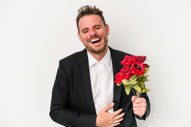 Jeune homme caucasien tenant un bouquet de fleurs isolé sur fond blanc en riant et en s'amusant.