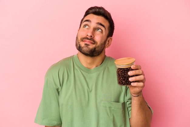 Jeune homme caucasien tenant une bouteille de café isolée sur un mur rose rêvant d'atteindre les objectifs et les buts