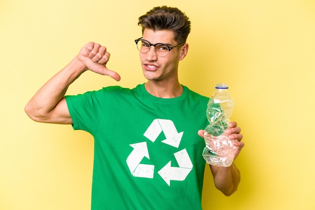 Jeune homme caucasien tenant une bouteille de plastique à recycler isolé sur fond jaune se sent fier et confiant, exemple à suivre.