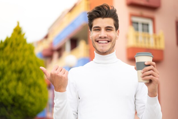 Jeune homme caucasien tenant un café à emporter à l'extérieur pointant vers le côté pour présenter un produit