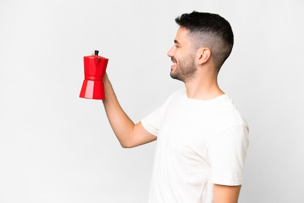 Jeune homme caucasien tenant une cafetière sur fond blanc isolé avec une expression heureuse