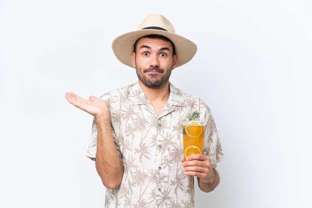 Jeune homme caucasien tenant un cocktail isolé sur fond blanc ayant des doutes tout en levant les mains
