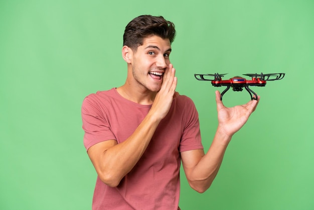 Jeune homme caucasien tenant un drone sur fond isolé chuchotant quelque chose