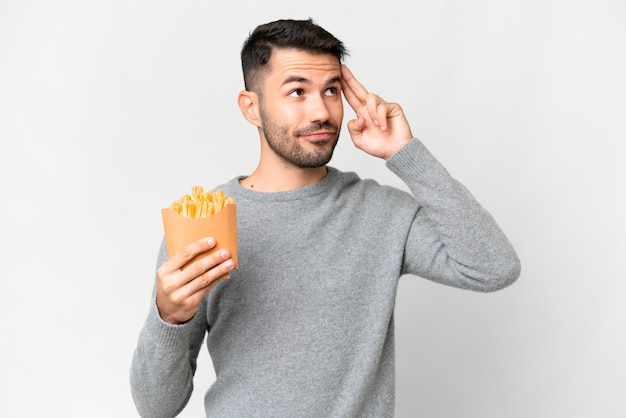 Jeune homme caucasien tenant des frites frites sur fond blanc isolé ayant des doutes et pensant