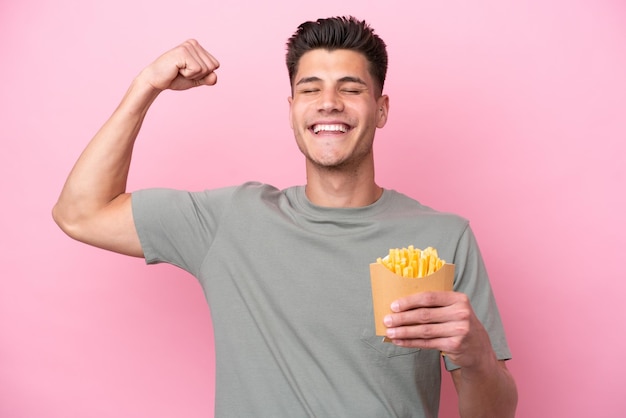 Jeune homme caucasien tenant des frites frites isolées sur fond rose faisant un geste fort