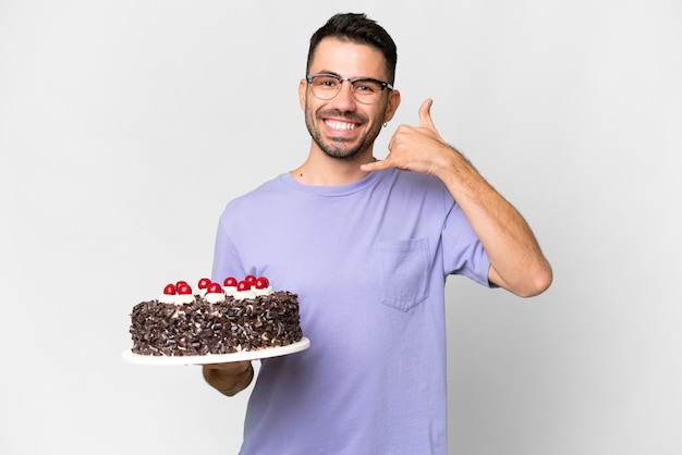 Jeune homme caucasien tenant un gâteau d'anniversaire isolé sur fond blanc faisant un geste de téléphone Appelez-moi signe de retour