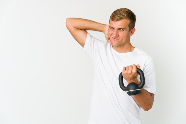 Jeune homme caucasien tenant un kettlebell isolé sur blanc heureux, souriant et joyeux.