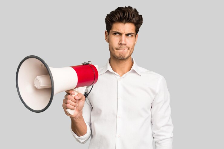 Photo jeune homme caucasien tenant un mégaphone isolé confus se sent douteux et incertain