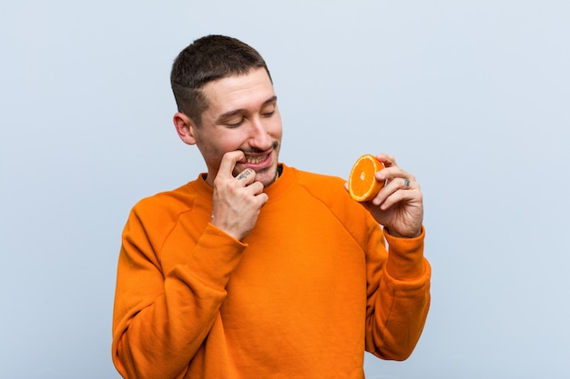 Jeune homme caucasien tenant une orange détendue en pensant à quelque chose en regardant un espace de copie.