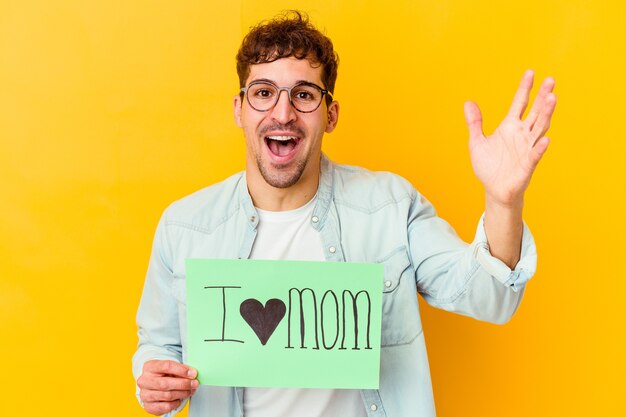 Jeune homme caucasien tenant une pancarte protéger notre planète isolée recevant une agréable surprise, excitée et levant les mains.