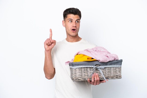 Jeune homme caucasien tenant un panier à linge isolé sur fond blanc en pensant à une idée pointant le doigt vers le haut