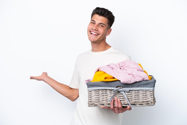 Jeune homme caucasien tenant un panier à linge isolé sur fond blanc tendant les mains sur le côté pour inviter à venir