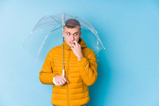 Jeune homme caucasien tenant un parapluie détendu penser à quelque chose en regardant un espace vide.