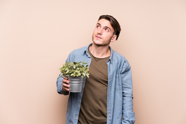 Jeune homme caucasien tenant une plante rêvant d'atteindre les objectifs et les buts
