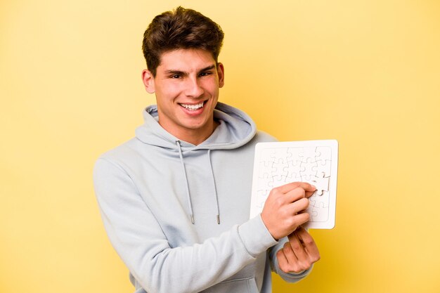 Jeune homme caucasien tenant un puzzle isolé sur fond jaune