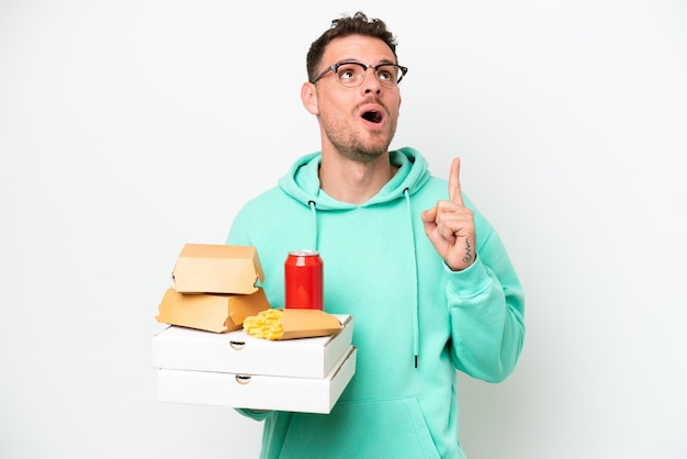 Jeune homme caucasien tenant restauration rapide isolé sur fond blanc pensant une idée pointant le doigt vers le haut