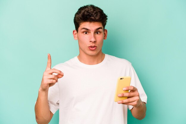 Jeune homme caucasien tenant un téléphone portable isolé sur fond bleu ayant une excellente idée de concept de créativité