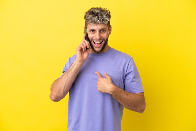 Jeune homme caucasien utilisant un téléphone portable isolé sur fond jaune avec une expression faciale surprise