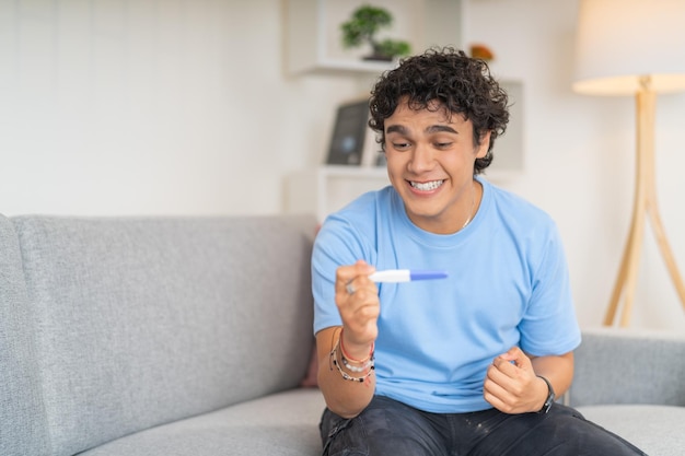 Photo jeune homme célébrant les résultats d'un test de grossesse assis seul à la maison