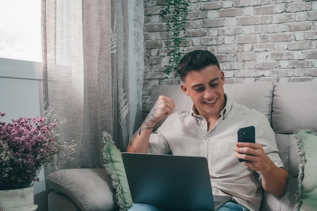 Un jeune homme célèbre une victoire sur son téléphone à la maison Adolescent euphorique s'amusant à regarder le football ou l'investissement sur smartphone et sur ordinateurxA