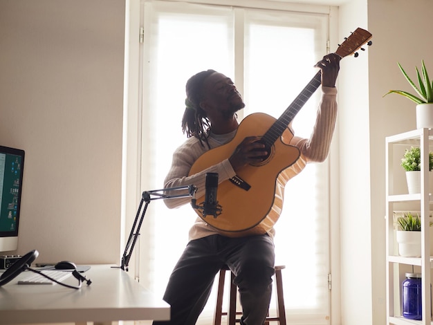 Un jeune homme chante et joue de la guitare tout en faisant un enregistrement audio à la maison