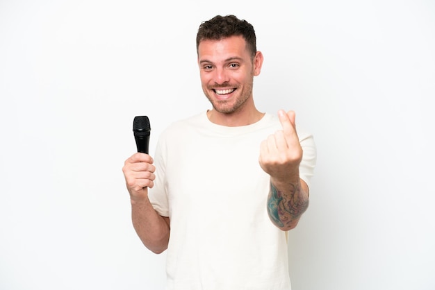 Jeune homme chanteur caucasien prenant un microphone isolé sur fond blanc faisant un geste d'argent