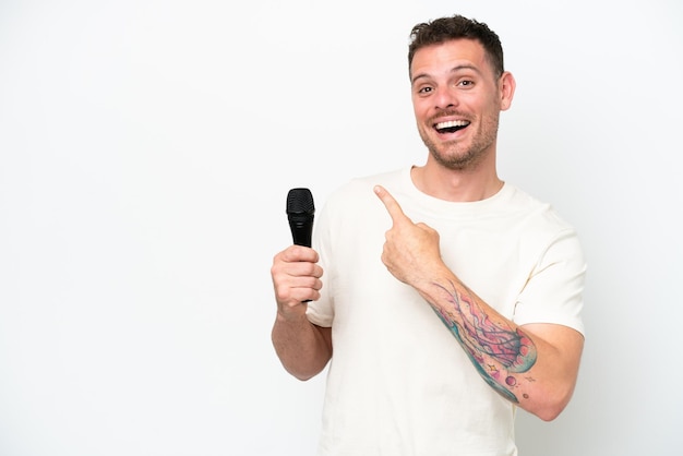 Jeune homme chanteur caucasien prenant un microphone isolé sur fond blanc pointant vers l'arrière