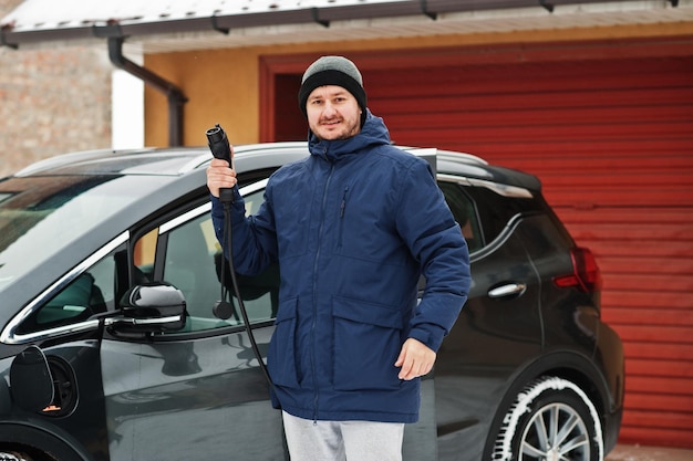 Jeune homme chargeant sa voiture électrique en hiver Concept de transport écologique