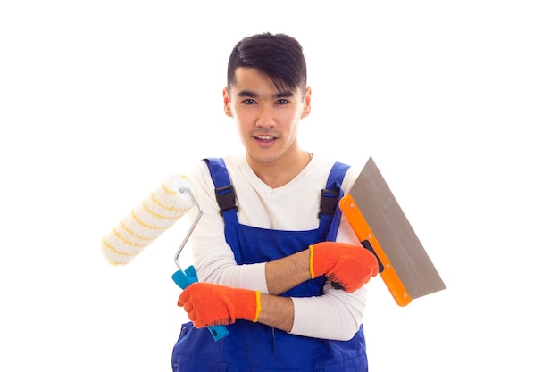 Jeune homme charmant en combinaison bleue avec des gants orange tenant une règle de rouleau de spatule et un tournevis