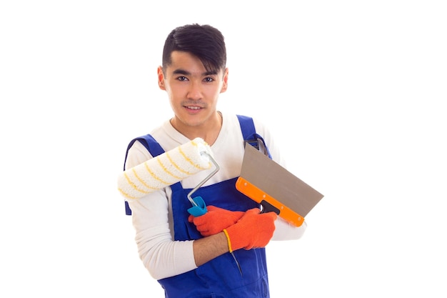 Jeune homme charmant en combinaison bleue avec des gants orange tenant une règle de rouleau de spatule et un tournevis