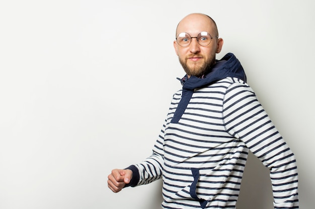 Jeune homme chauve avec une barbe à lunettes, un pull à capuche en marchant sur un blanc isolé.