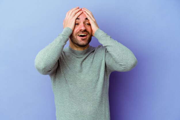 Jeune homme chauve caucasien isolé sur fond violet rit joyeusement en gardant les mains sur la tête. Concept de bonheur.