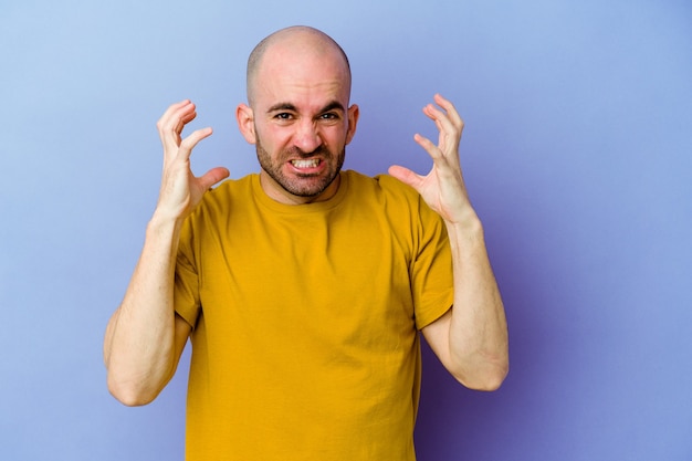 Jeune homme chauve caucasien isolé sur mur violet hurlant de rage.