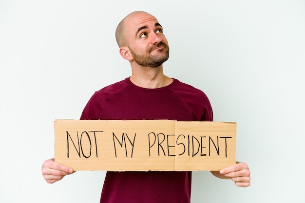 Jeune homme chauve caucasien tenant une pancarte pas mon président isolé sur un mur blanc rêvant d'atteindre les objectifs et les buts