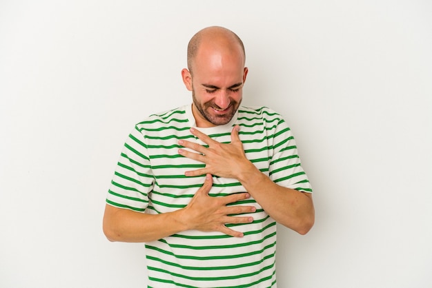 Jeune homme chauve isolé sur fond blanc rit joyeusement et s'amuse en gardant les mains sur le ventre.