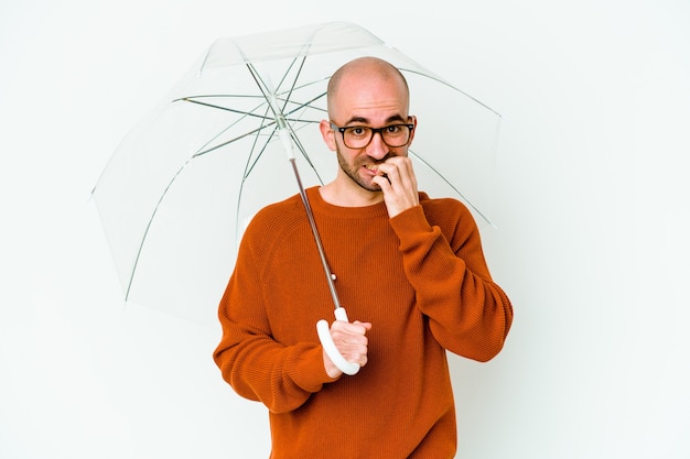 Jeune homme chauve tenant un parapluie isolé des ongles mordants, nerveux et très anxieux.