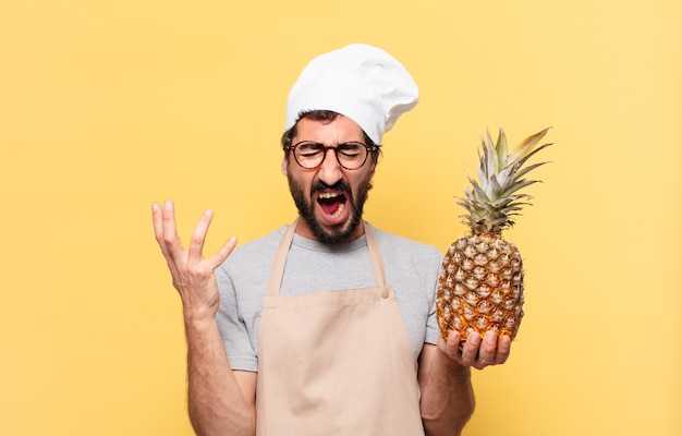 Jeune homme chef barbu expression en colère tenant un ananas