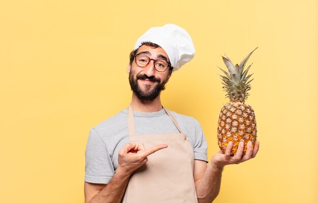 Jeune homme chef barbu pointant ou montrant la tenue d'un ananas