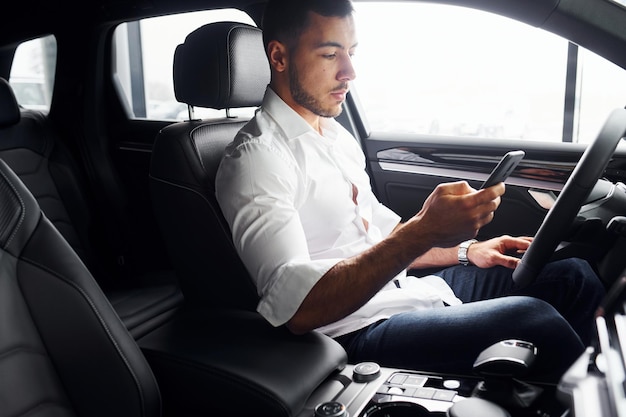 Jeune homme en chemise blanche est assis à l'intérieur d'une nouvelle automobile moderne