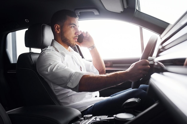 Jeune homme en chemise blanche est assis à l'intérieur d'une nouvelle automobile moderne