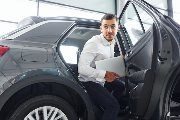 Jeune homme en chemise blanche est à l'intérieur avec une nouvelle automobile moderne