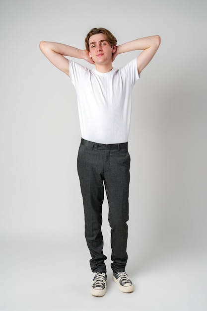 Un jeune homme en chemise blanche et en pantalon noir se tient détendu avec les mains derrière la tête