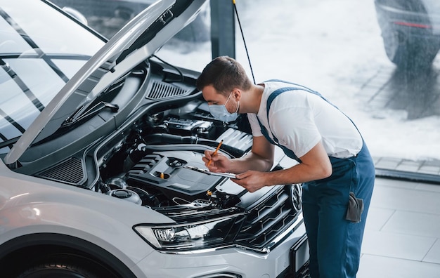 Jeune homme en chemise blanche et uniforme bleu répare l'automobile