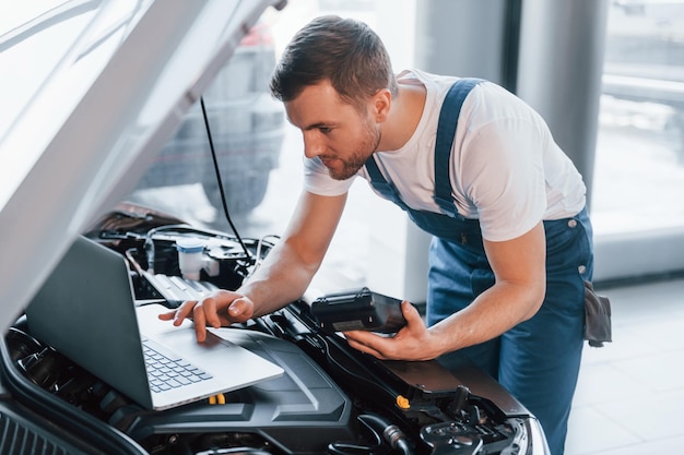 Jeune homme en chemise blanche et uniforme bleu répare une automobile