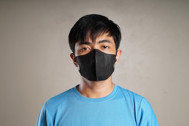 Un jeune homme en chemise bleu clair portant un masque noir regarde la caméra